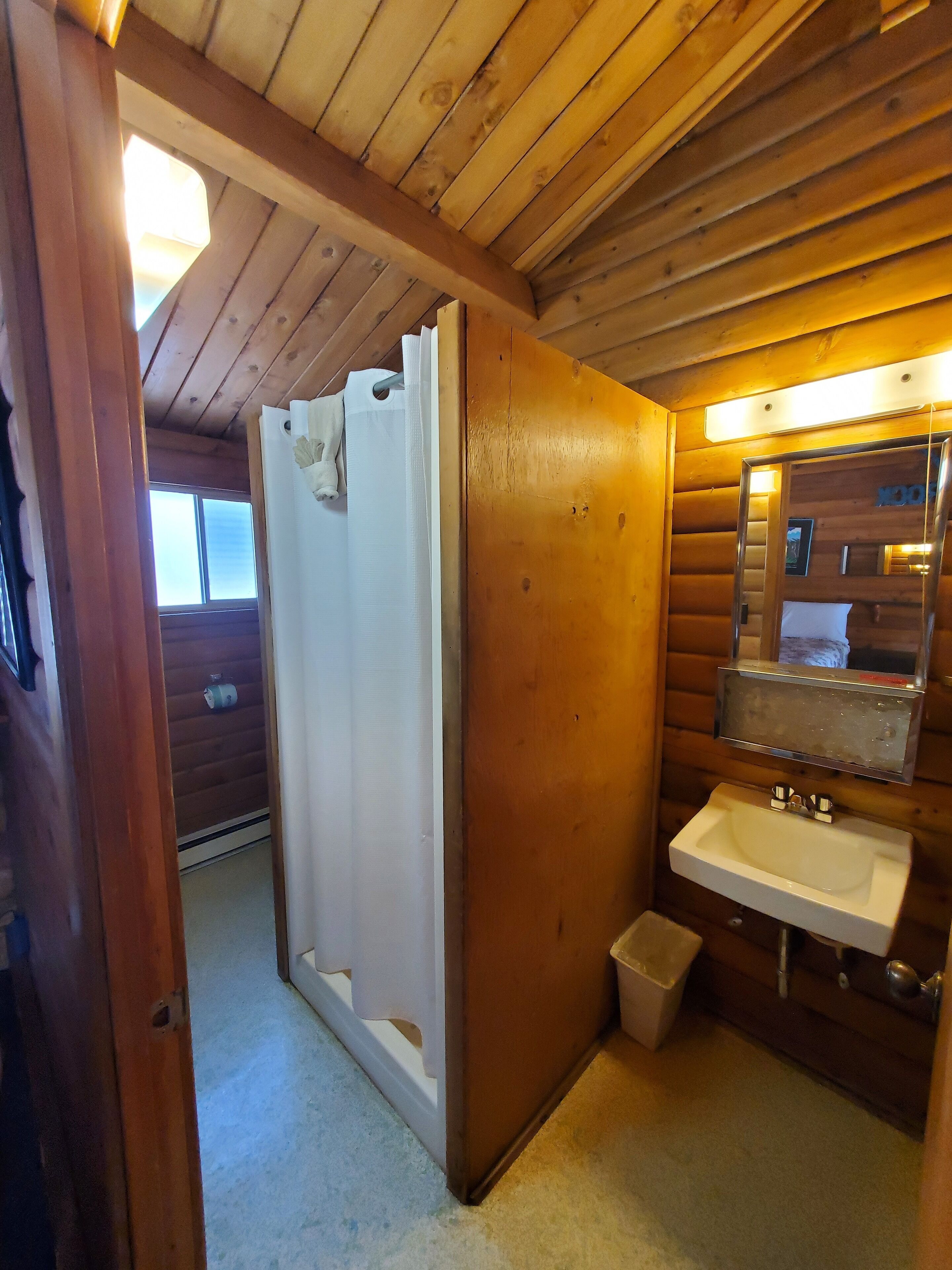 A wooden cabin bathroom with a white sink, a mirror, and a shower curtain.