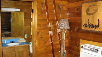 A wooden cabin interior with a wooden wall, a mirror, a sink, and a heater.