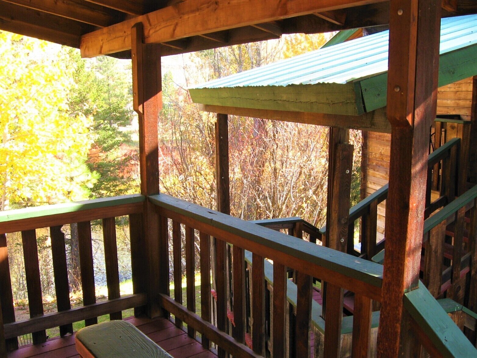 A wooden deck with a railing, overlooking a forested area with autumn foliage.