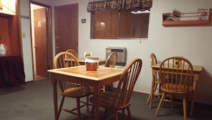 A dining area with a wooden table and chairs, an air conditioning unit, and a window with blinds. - Caboose Motel (Libby)