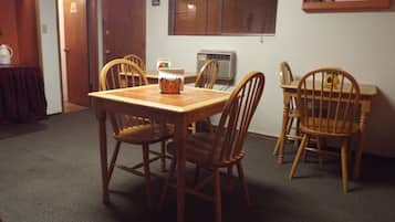 Een eetruimte met een houten tafel en stoelen, een airconditioning en een raam met zonwering.