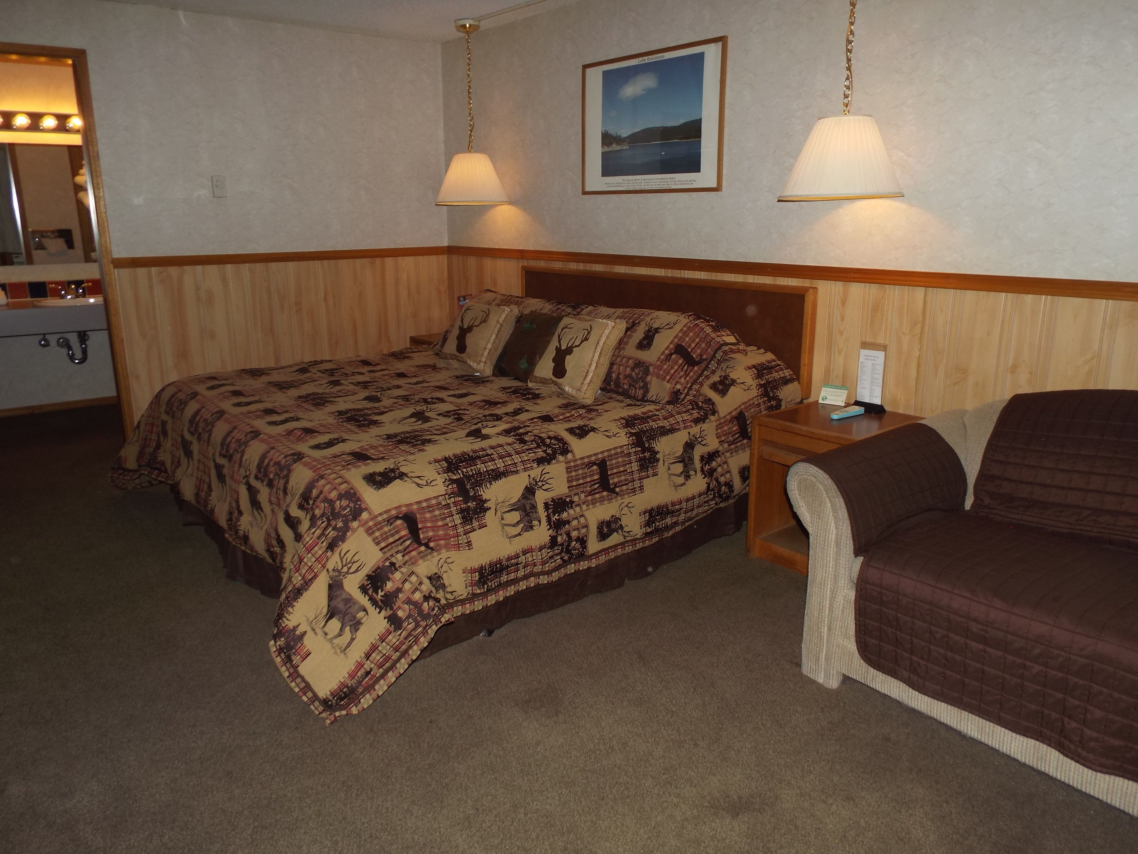 Ett hotellrum med en säng, ett nattduksbord, en lampa, en stol och en spegel.