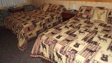 A hotel room with two beds, each with a patterned blanket featuring animal prints. There is a bedside table with a lamp, a wall-mounted clock, and a framed picture above the bed.