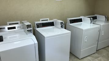 Een rij witte voorladingswasmachines in een wasserij met een beige muur en betegelde vloer.