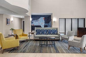 A modern lobby with a sofa, armchairs, a coffee table, and a large abstract wall art piece.