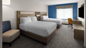 A hotel room with two beds, a desk, a chair, a TV, and a window with blinds.