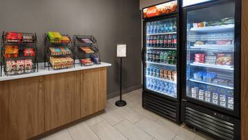 Zona de máquinas expendedoras con Coca-Cola bien fría y otras bebidas, cajas de aperitivos y un refrigerador Coca-Cola.
