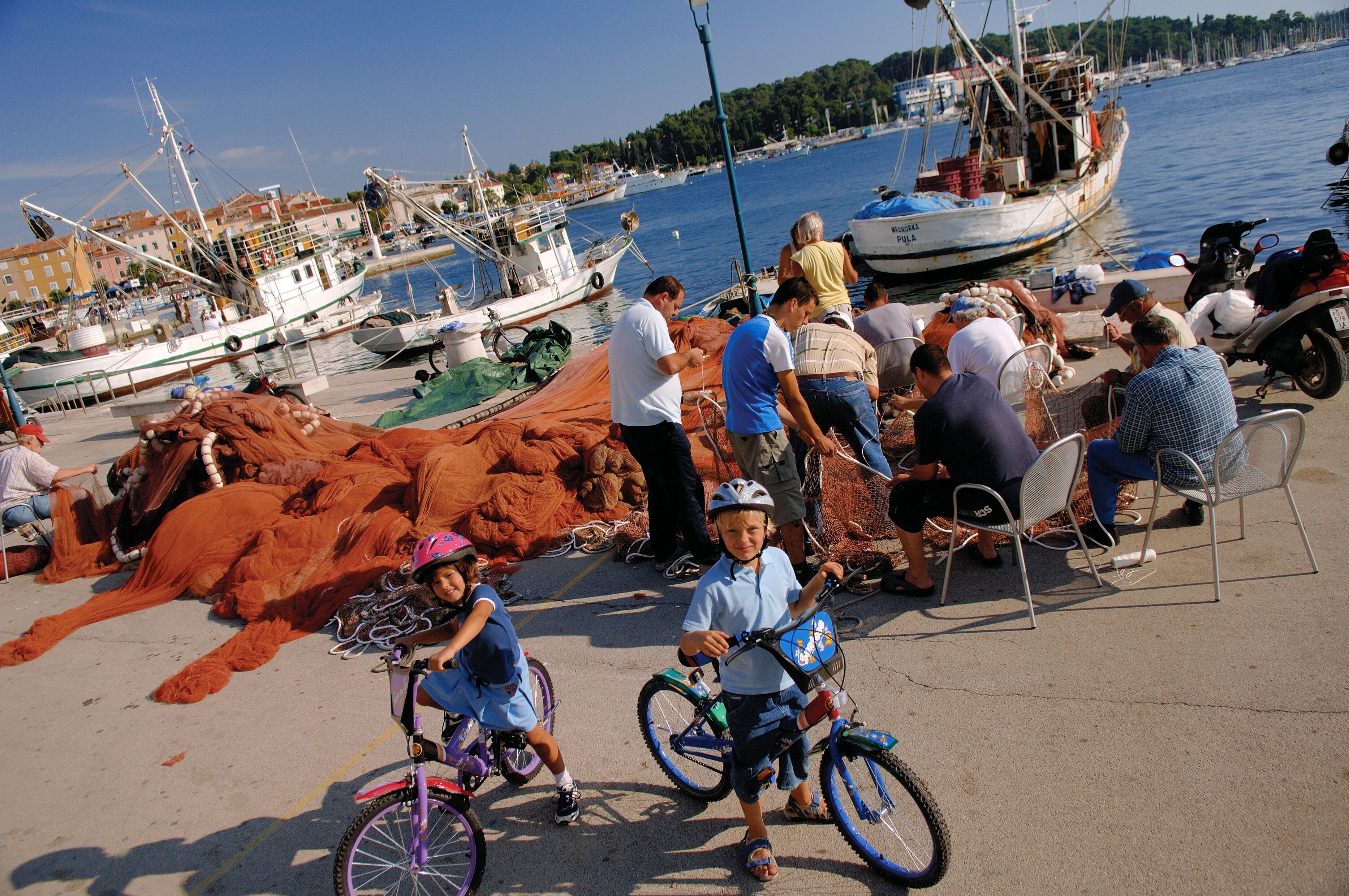 A harbor with boats, people, and children on bicycles.