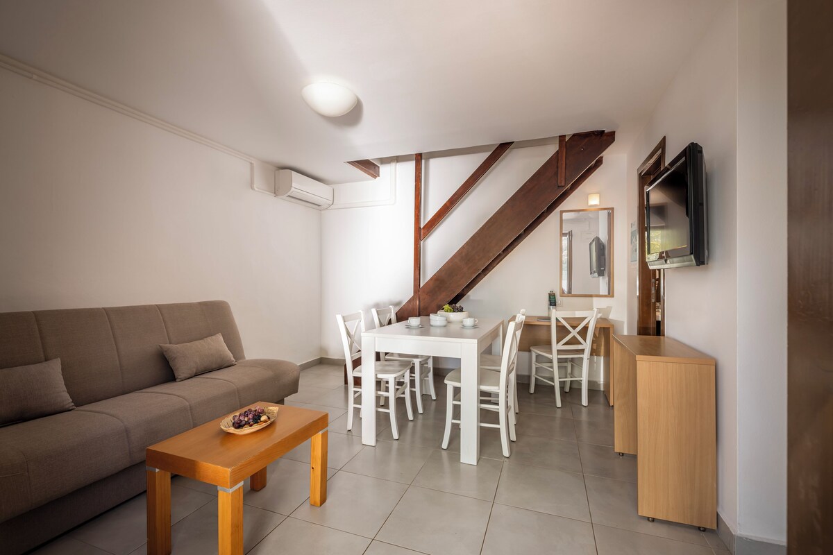 A modern living room with a sofa, dining table, and chairs. There is a staircase leading to an upper level.