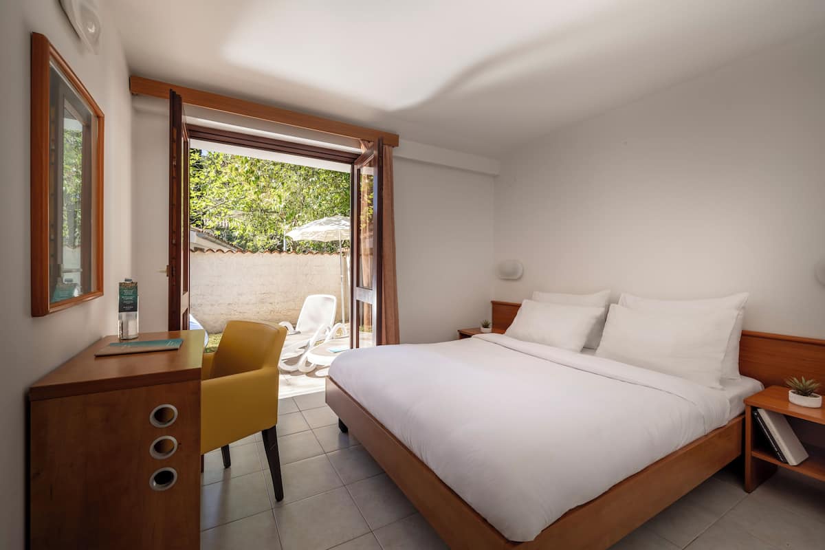 Un dormitorio con una cama grande, un escritorio de madera, una silla amarilla y un ventanal corredero que da a un espacio exterior.