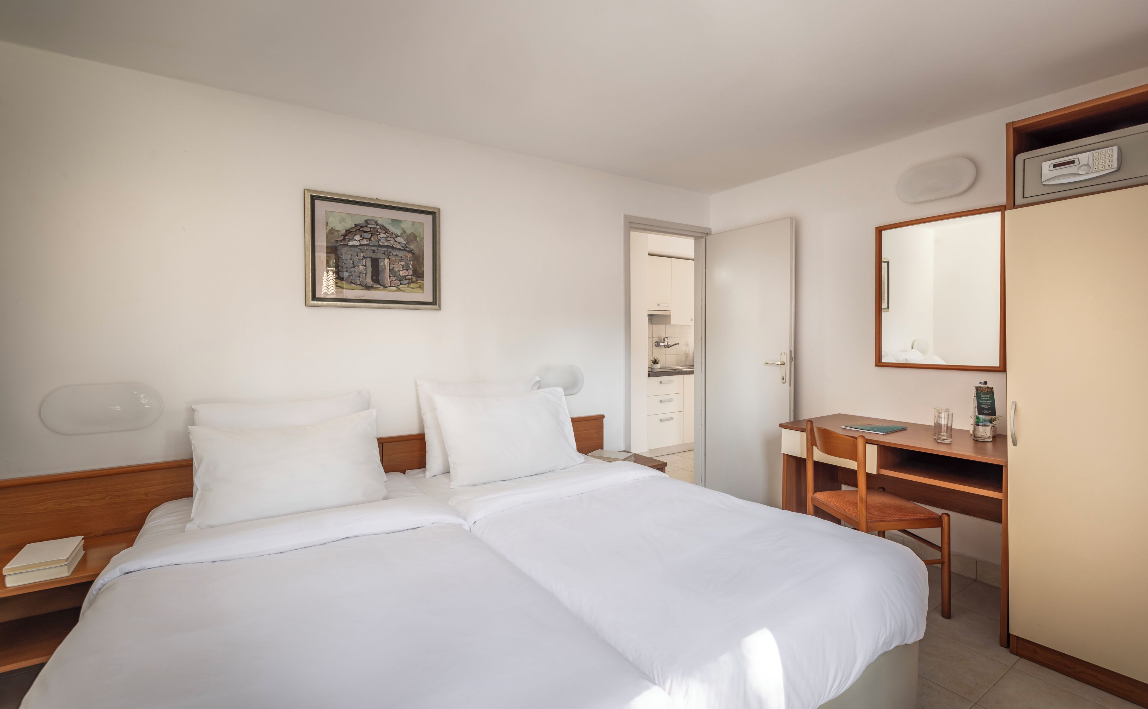 Habitación de hotel con cama, escritorio, silla, espejo y un cuadro en la pared.