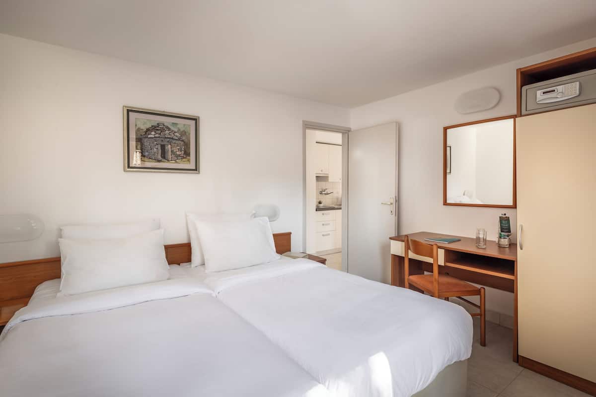 Habitación de hotel con cama, escritorio, silla, espejo y un cuadro en la pared.