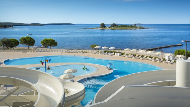 A resort pool with water slides, lounge chairs, and a view of the sea.