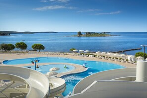 A resort pool with water slides, lounge chairs, and a view of the sea. - Maistra Select Villas Rubin Resort  (Rovinj)