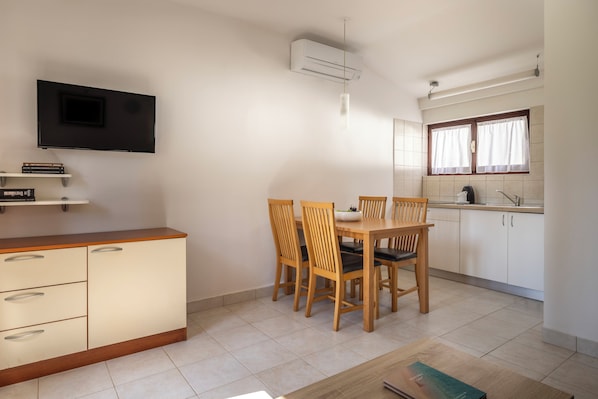 Una cocina funcional con mesa, sillas, televisor montado en la pared y ventana con cortinas.