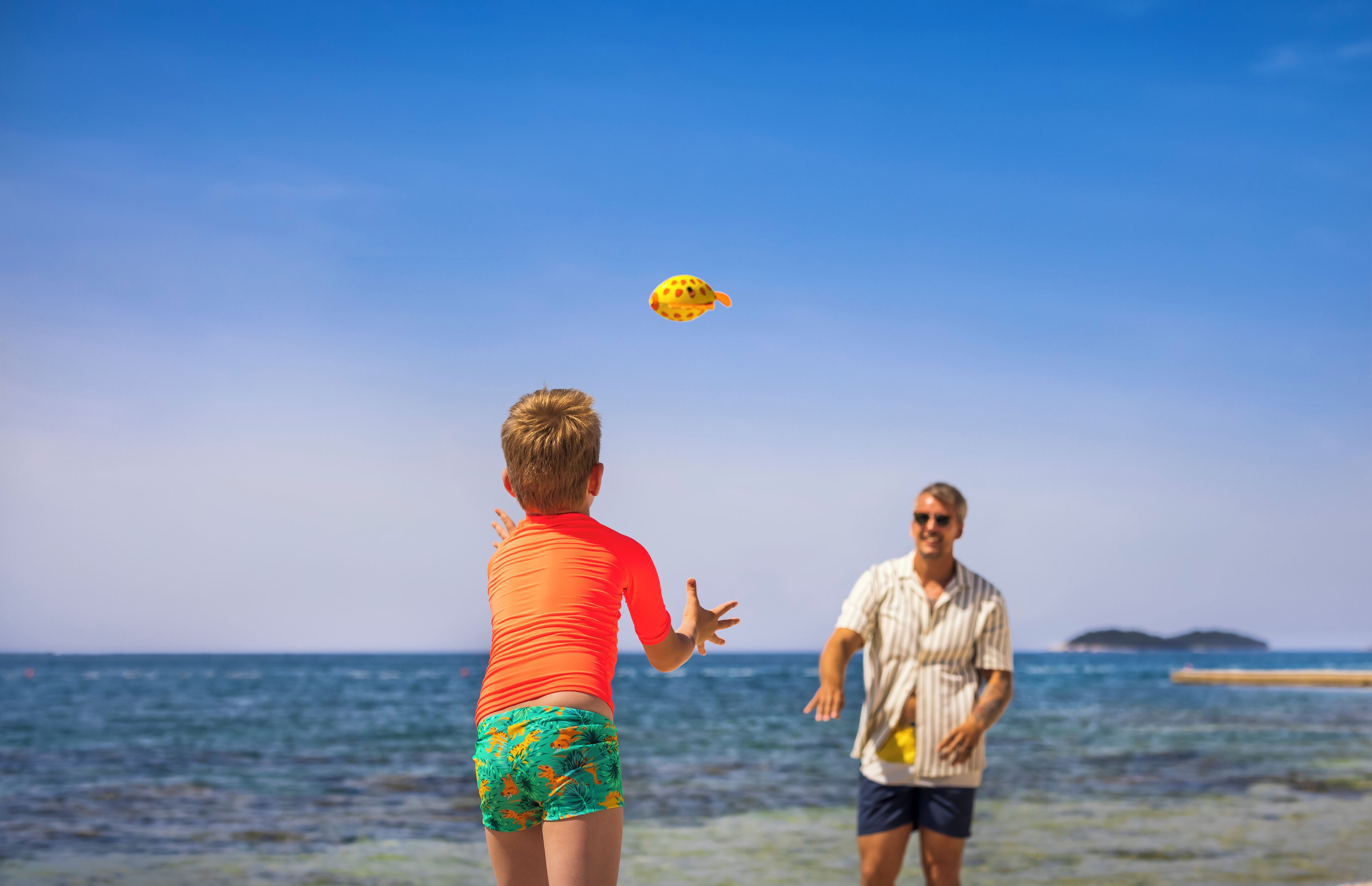 A beach scene with two people playing with a yellow frisbee.
