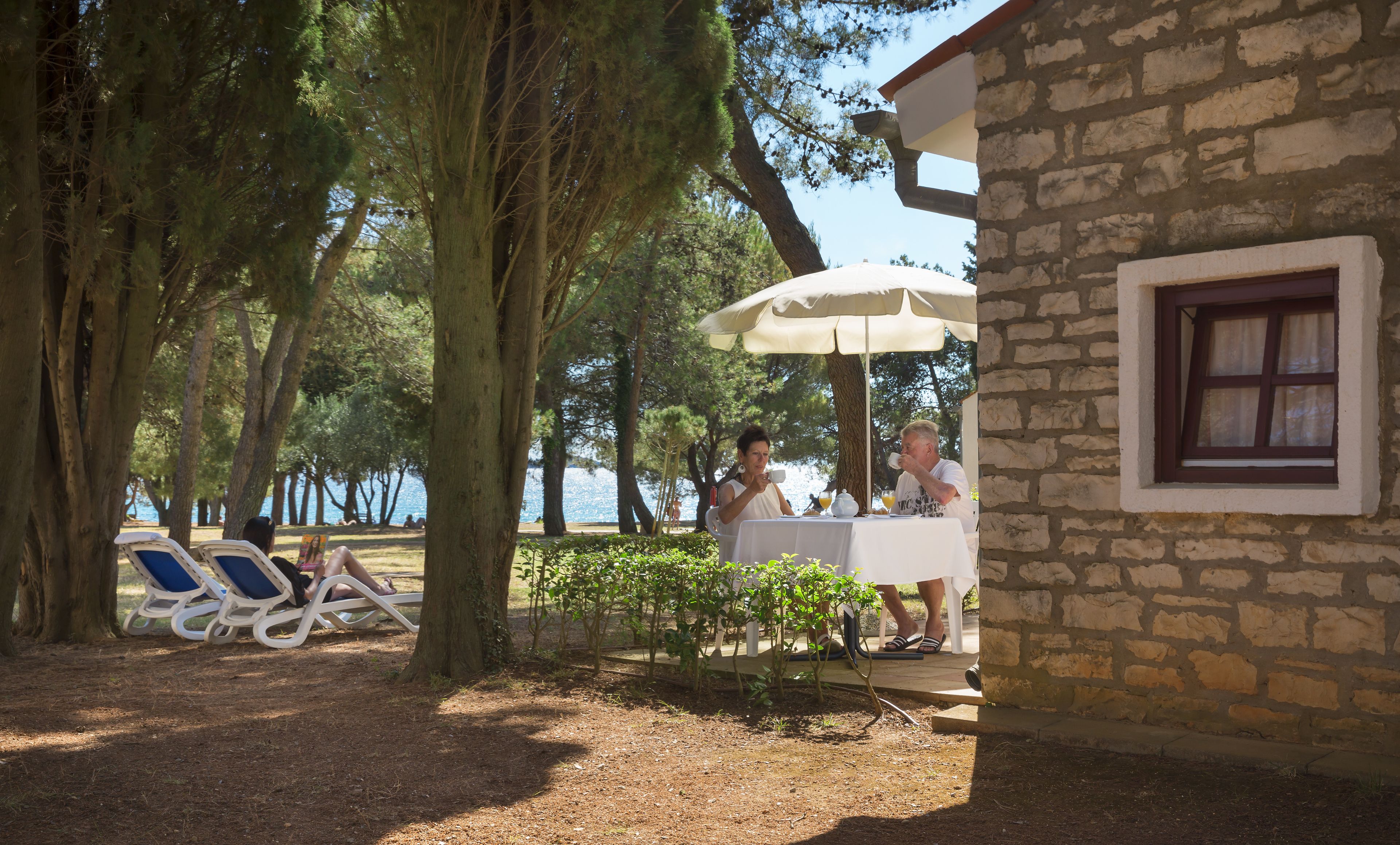A stone building with a window, a table with an umbrella, and a view of the sea.