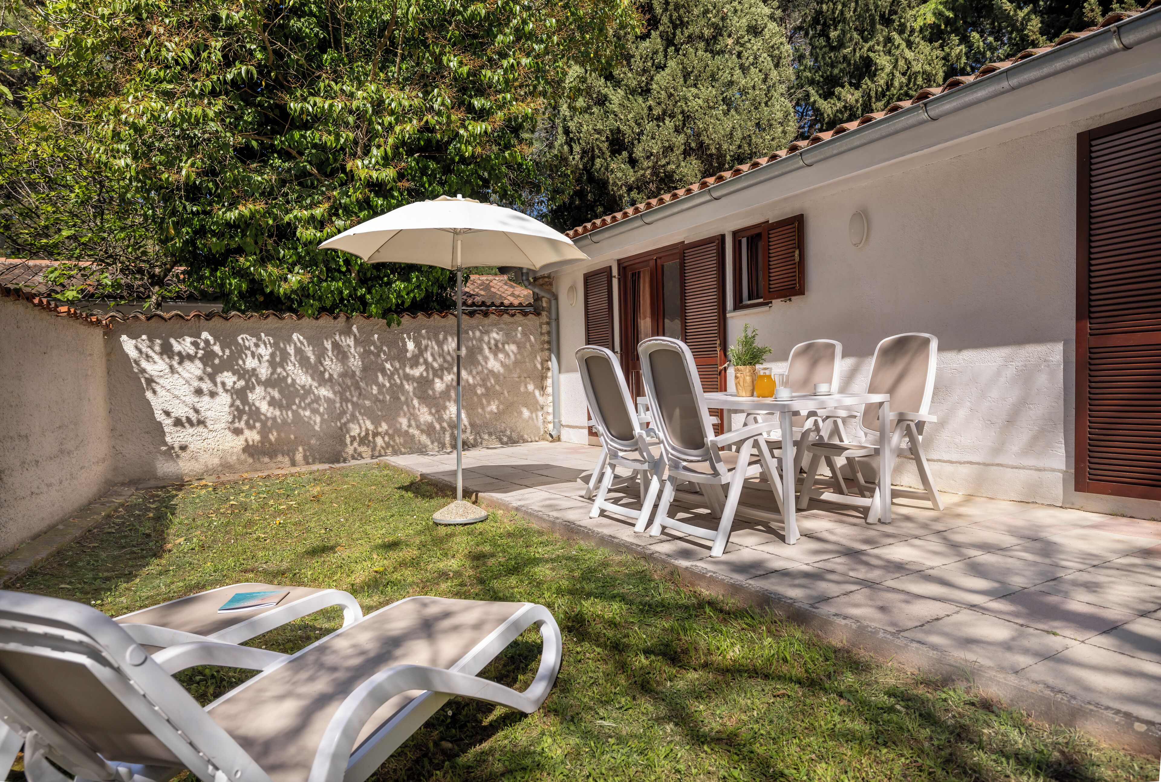 A patio with white chairs, a table, and an umbrella.