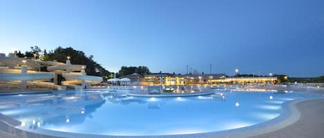 A swimming pool area with a water slide, lounge chairs, and a building with outdoor seating.