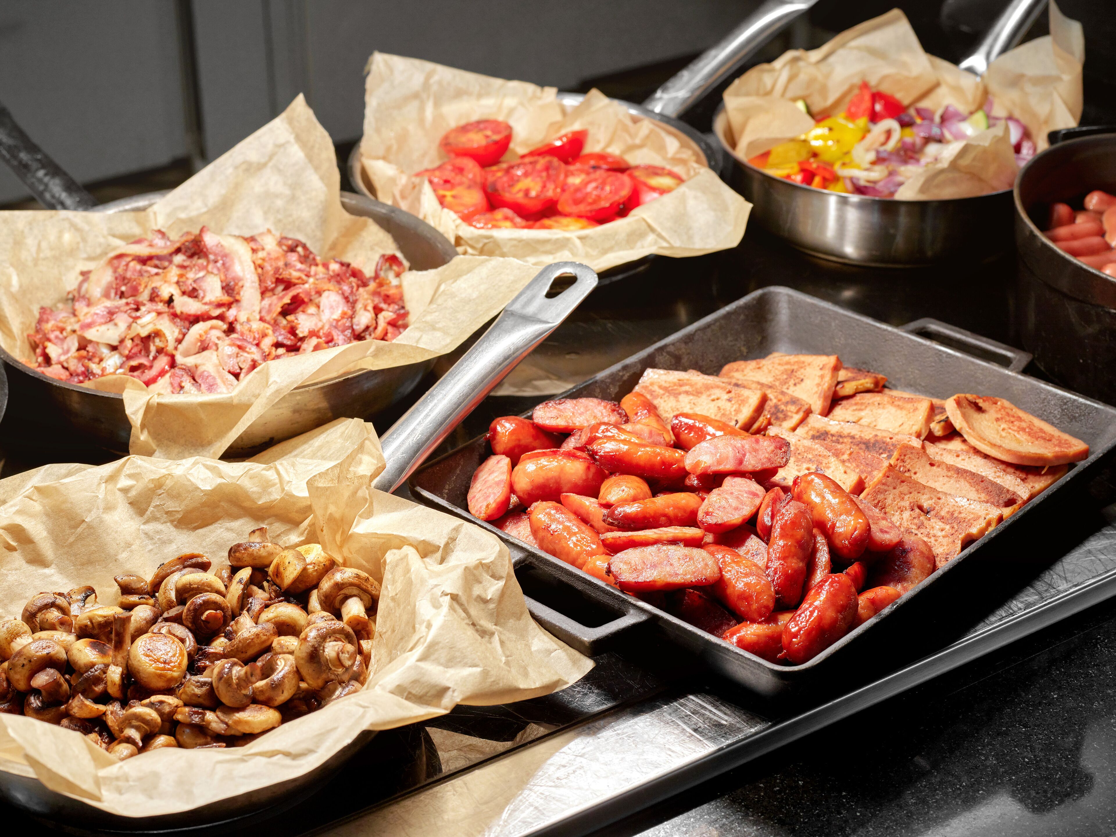 Een buffet met diverse soorten eten, zoals worstjes, champignons en plakjes tomaat.