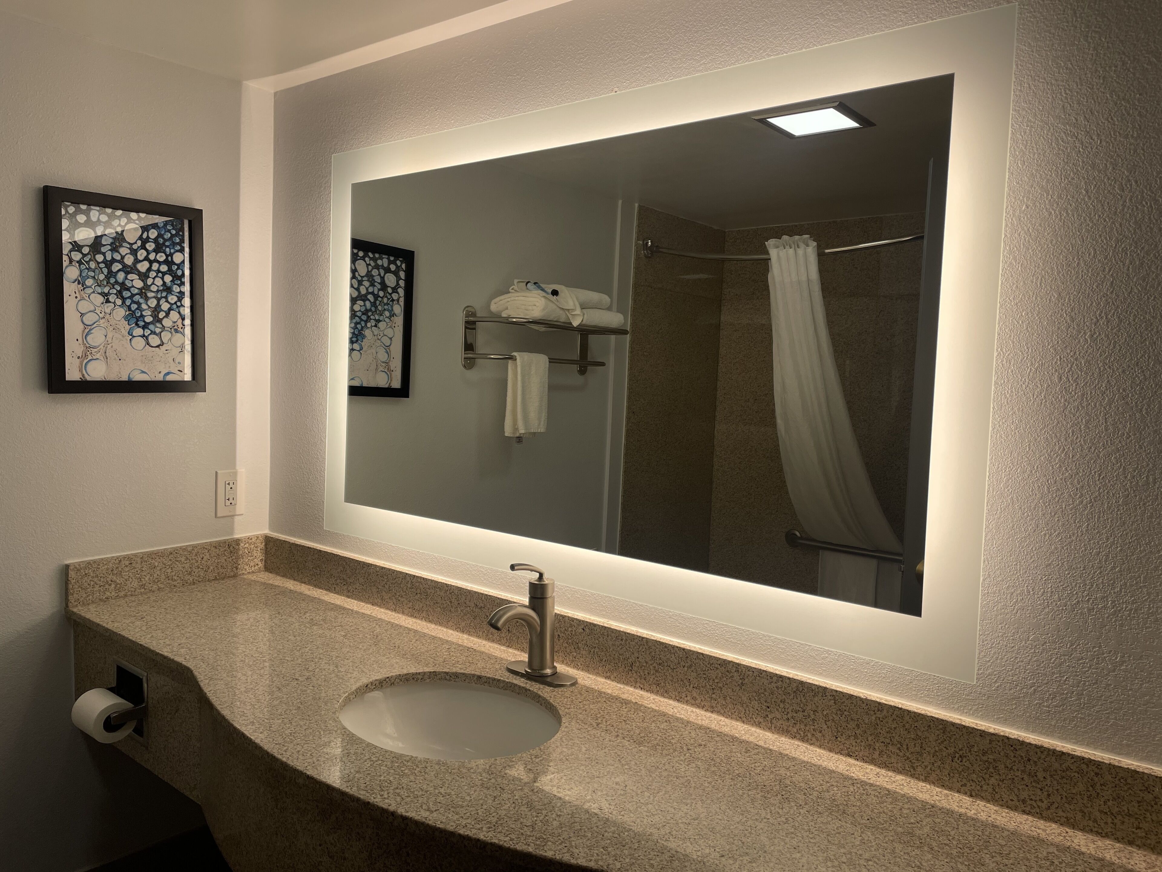 A bathroom with a large mirror, granite countertop, and a shower curtain.