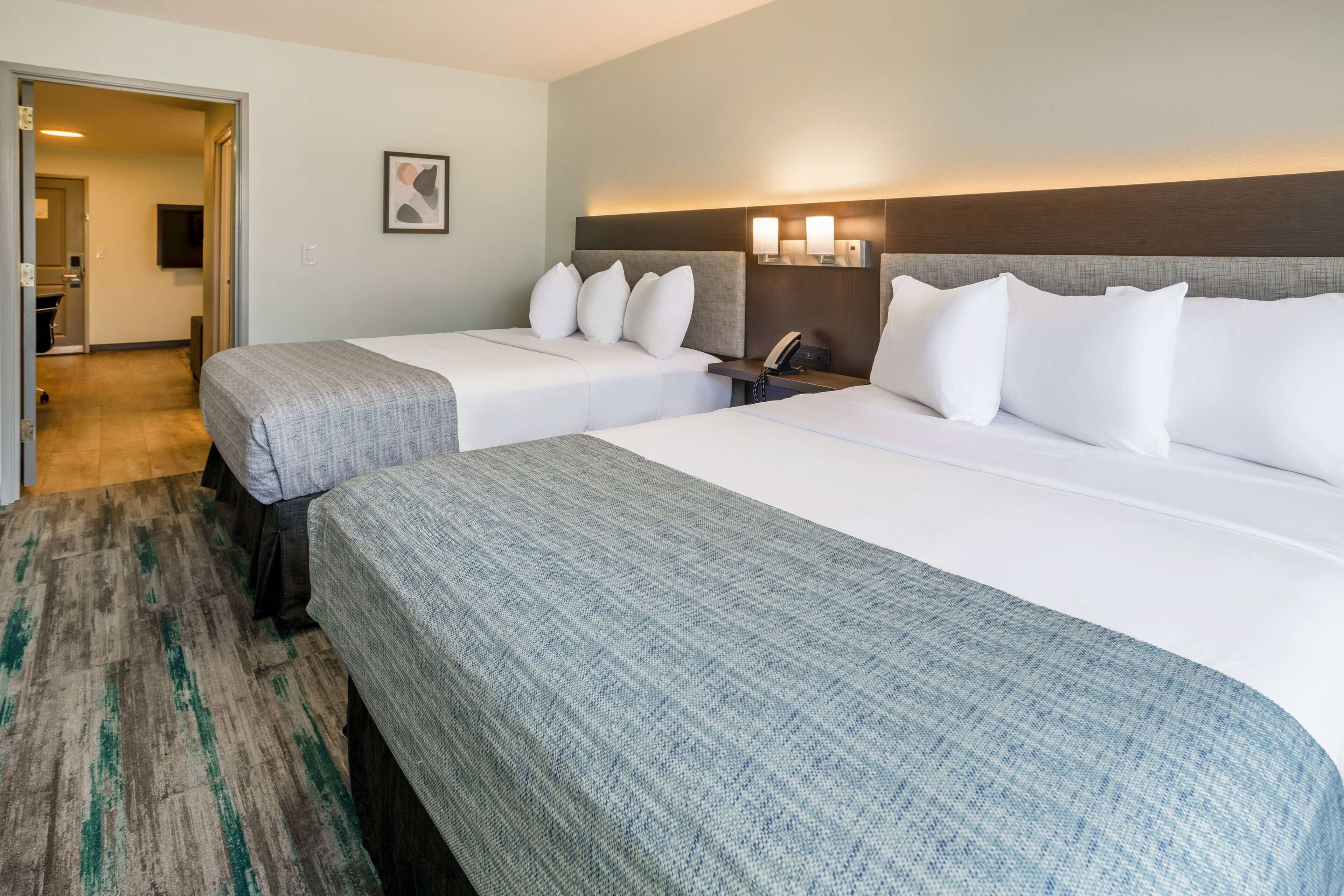 A hotel room with two beds, a wooden headboard, a flat-screen TV, and a small desk with a phone.