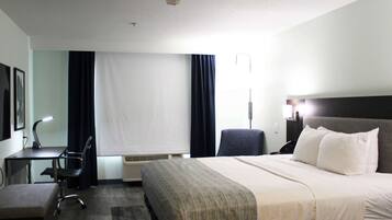 A hotel room with a bed, a desk, a chair, and a lamp.