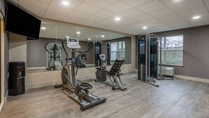 Une salle de sport équipée de divers appareils d’exercice, d’un grand miroir et d’une fenêtre donnant sur une maison.