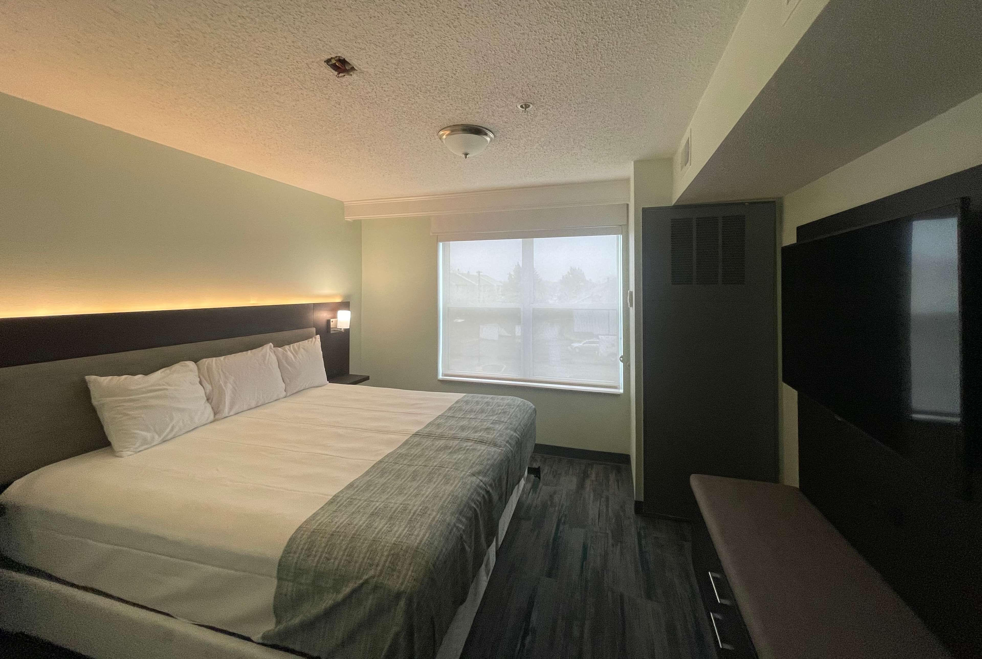 Una habitación de hotel con cama, televisión, ventana y puerta.