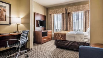 A hotel room with a desk, chair, TV, bed, and curtains.