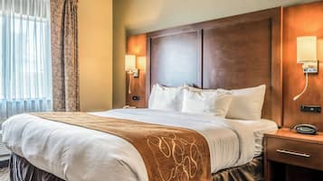 A hotel room with a large bed, wooden headboard, bedside lamps, and a nightstand with a clock.