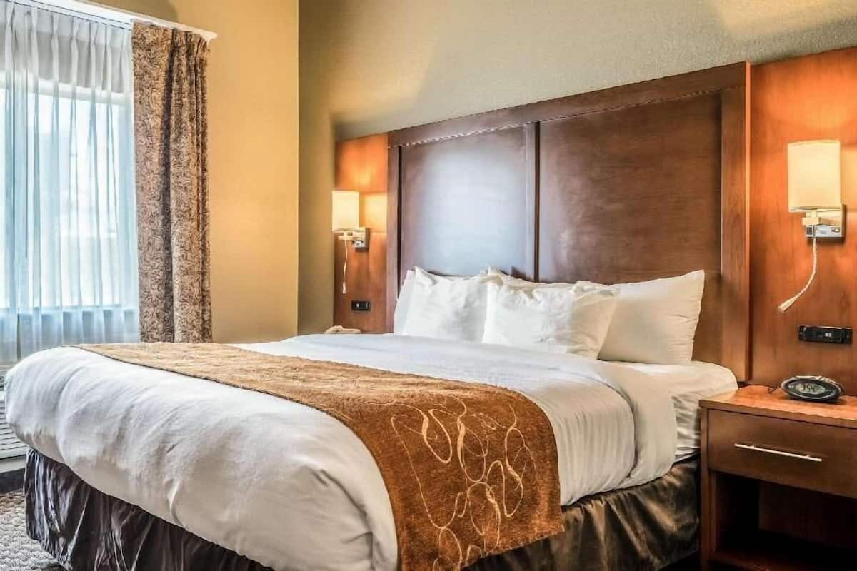 Ein Hotelzimmer mit einem großen Bett, zwei Nachttischlampen, einem Nachttisch und einem mit Vorhängen versehenen Fenster.