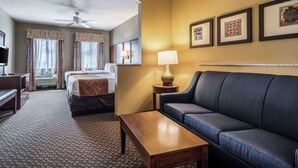 Een hotelkamer met een bed, een bank, een bureau, een lamp en ingelijste foto’s aan de muur.