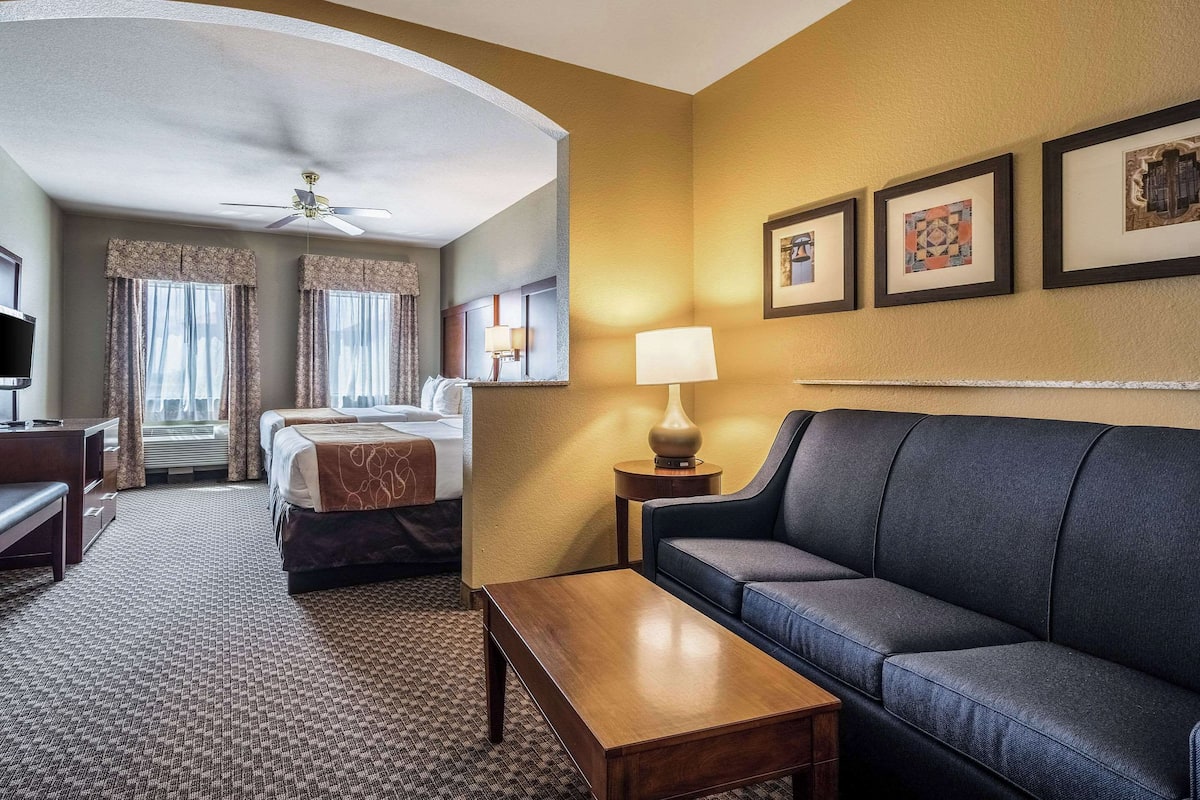 Ein Hotelzimmer mit Bett, einer Couch, einem Schreibtisch, einer Lampe und gerahmten Bildern an der Wand.