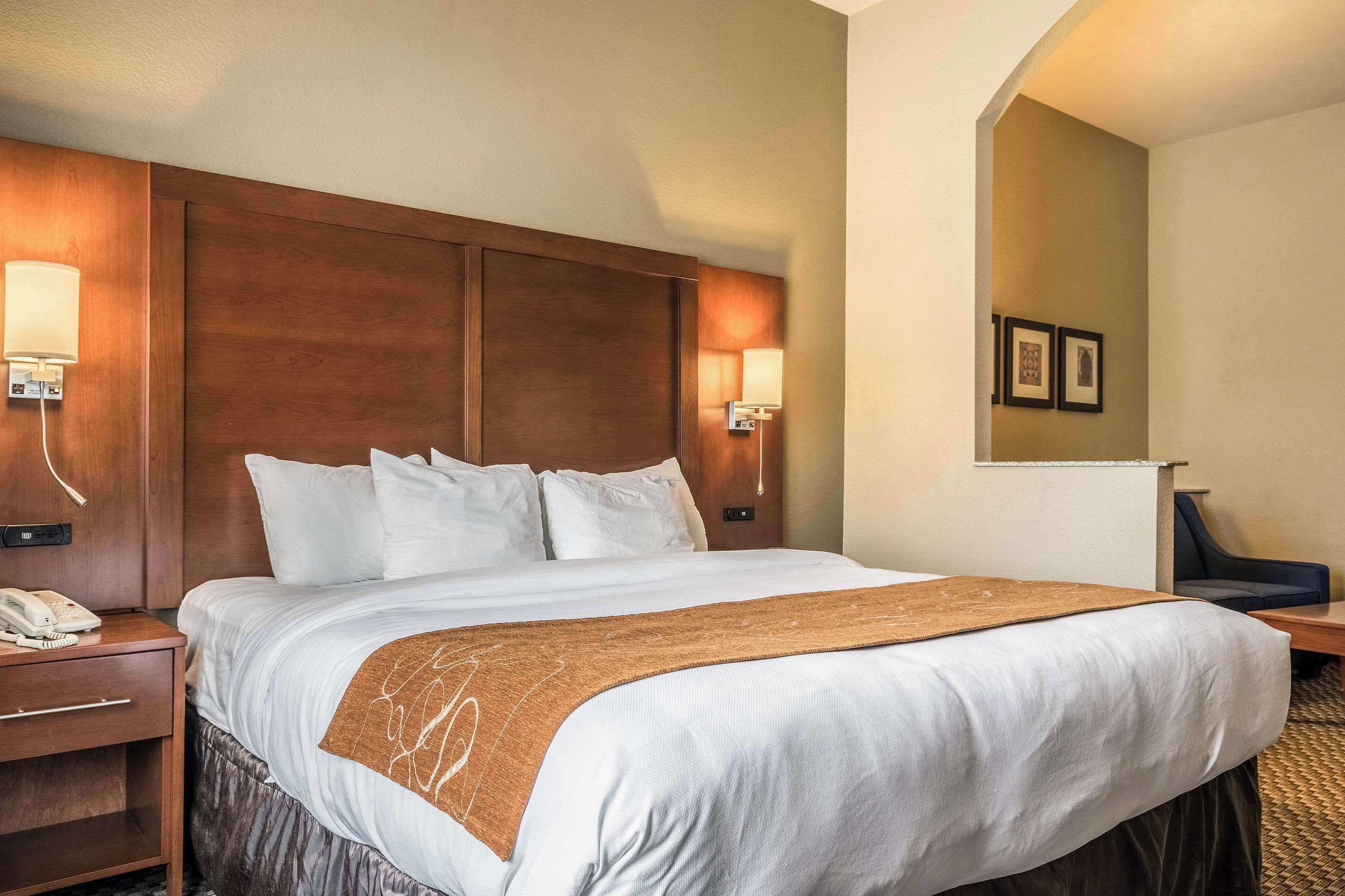 Une chambre d’hôtel avec un grand lit, une tête de lit en bois, des lampes de chevet, un téléphone et un petit bureau avec une chaise.
