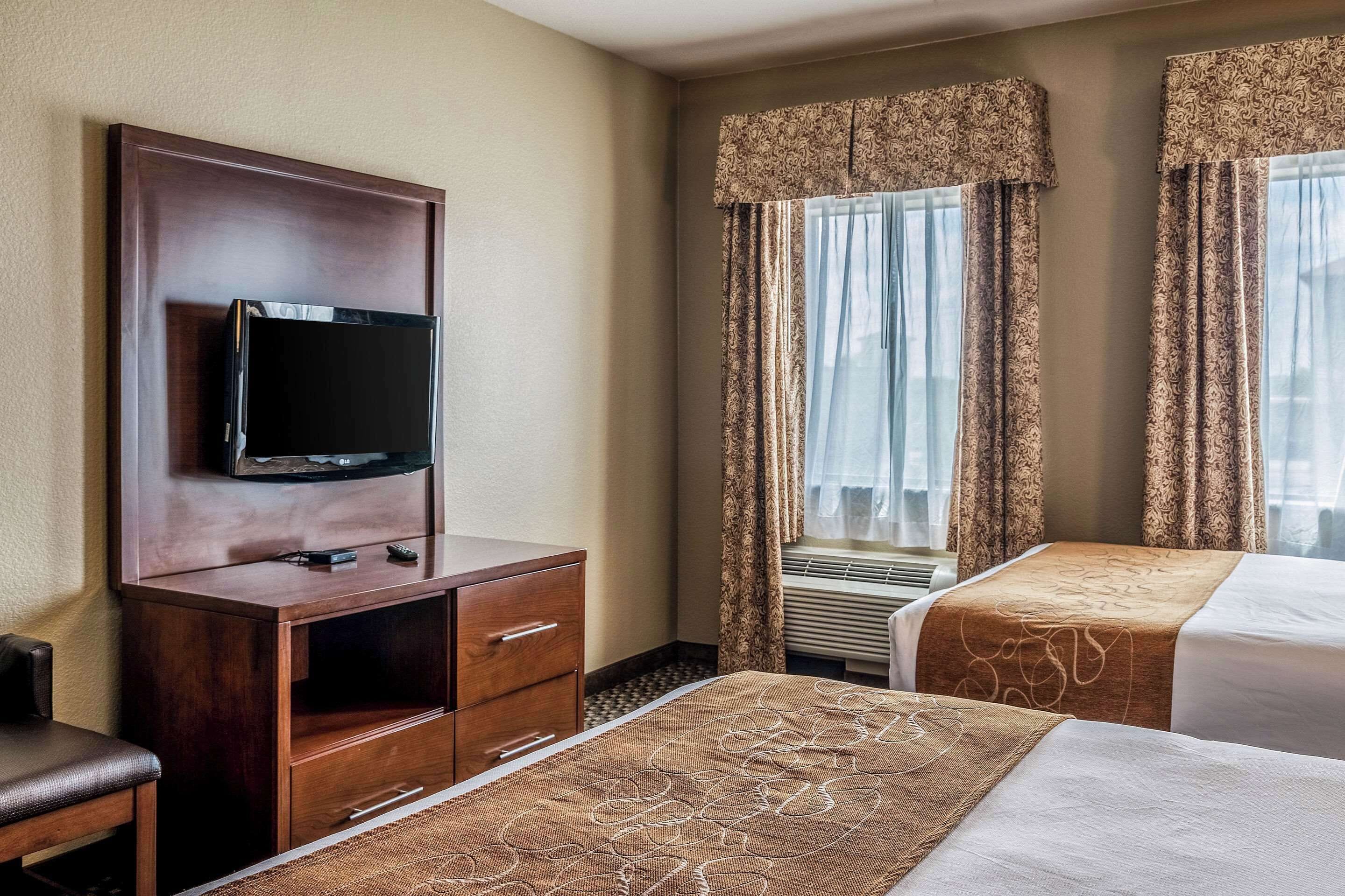 Quarto de hotel com televisão em um armário de madeira, duas camas com colchas estampadas e uma janela com cortinas.