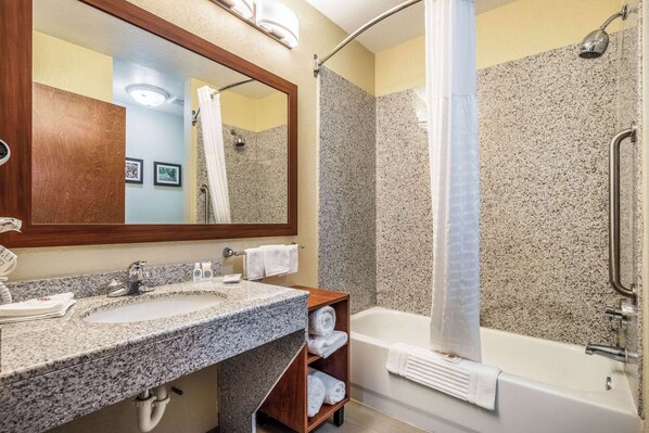 A bathroom with a granite countertop sink, a wooden vanity, a white bathtub, and a shower with a glass door.