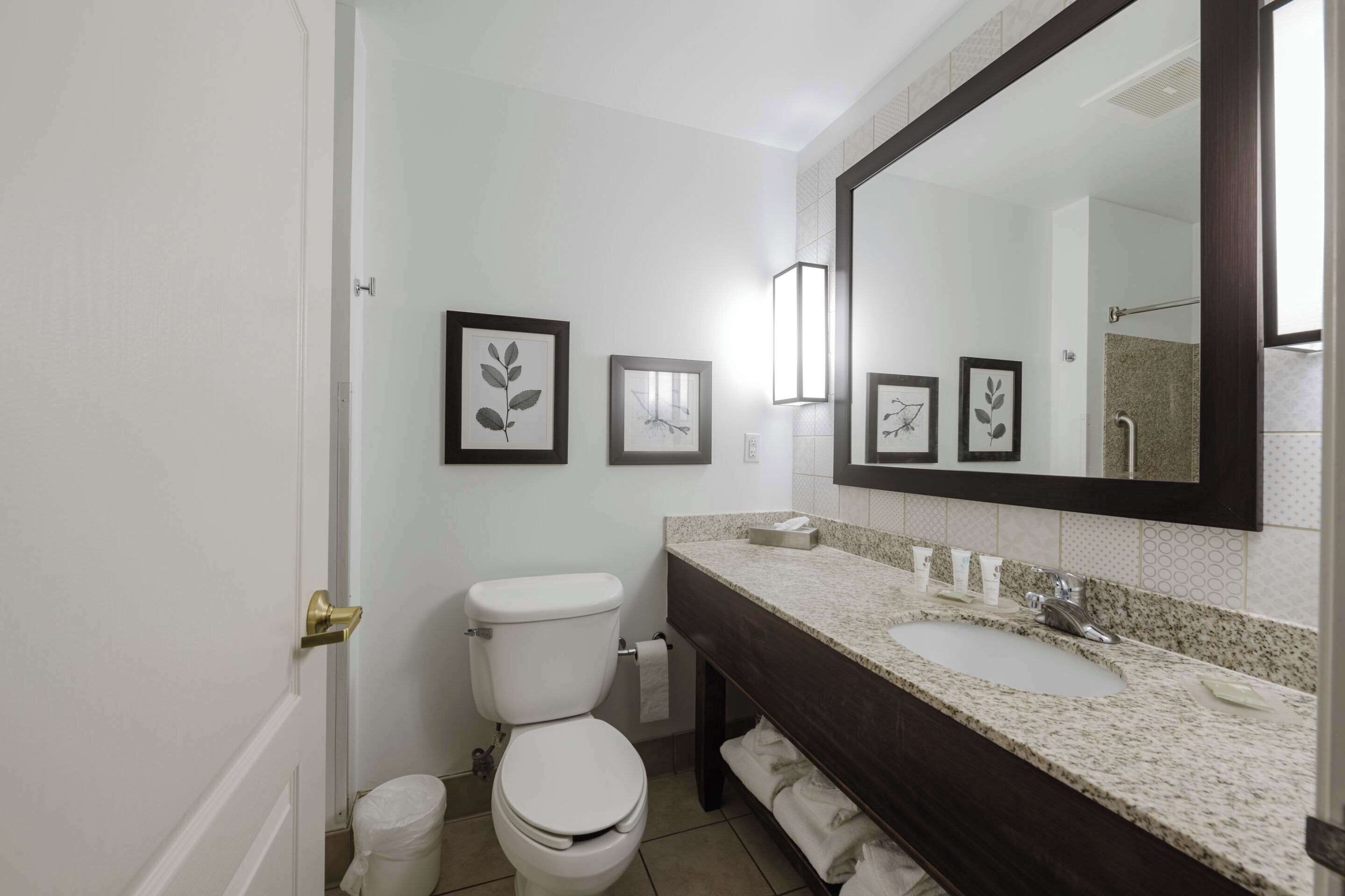 Un baño con inodoro blanco, un lavabo con encimera oscura y fotografías enmarcadas en la pared.