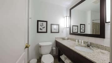 Un baño con inodoro blanco, un lavabo con encimera oscura y fotografías enmarcadas en la pared.