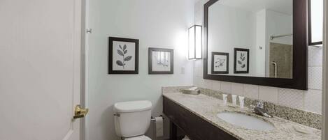 Un baño con inodoro blanco, un lavabo con encimera oscura y fotografías enmarcadas en la pared.