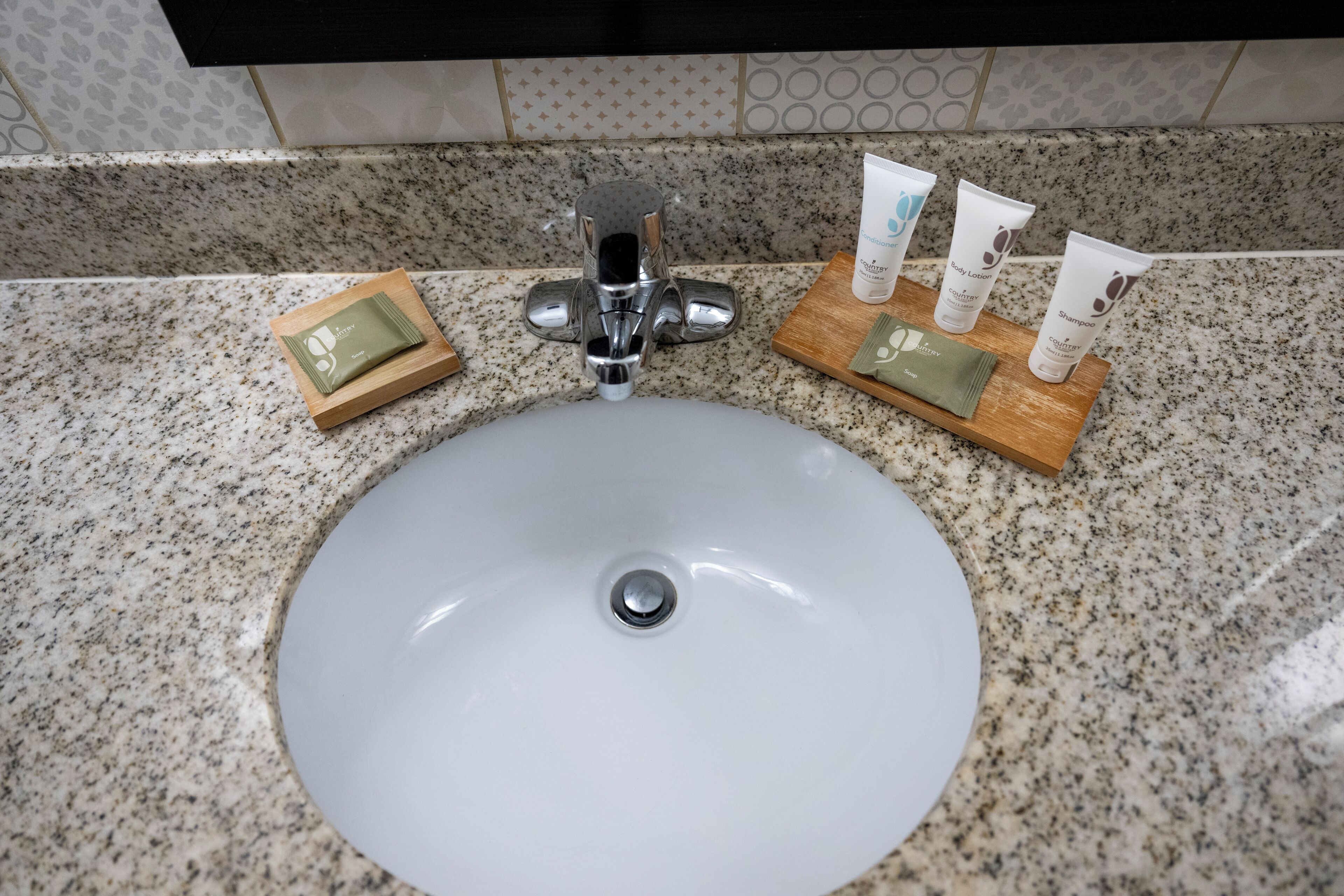 A bathroom sink with a granite countertop, a chrome faucet, and toiletries on a wooden tray.