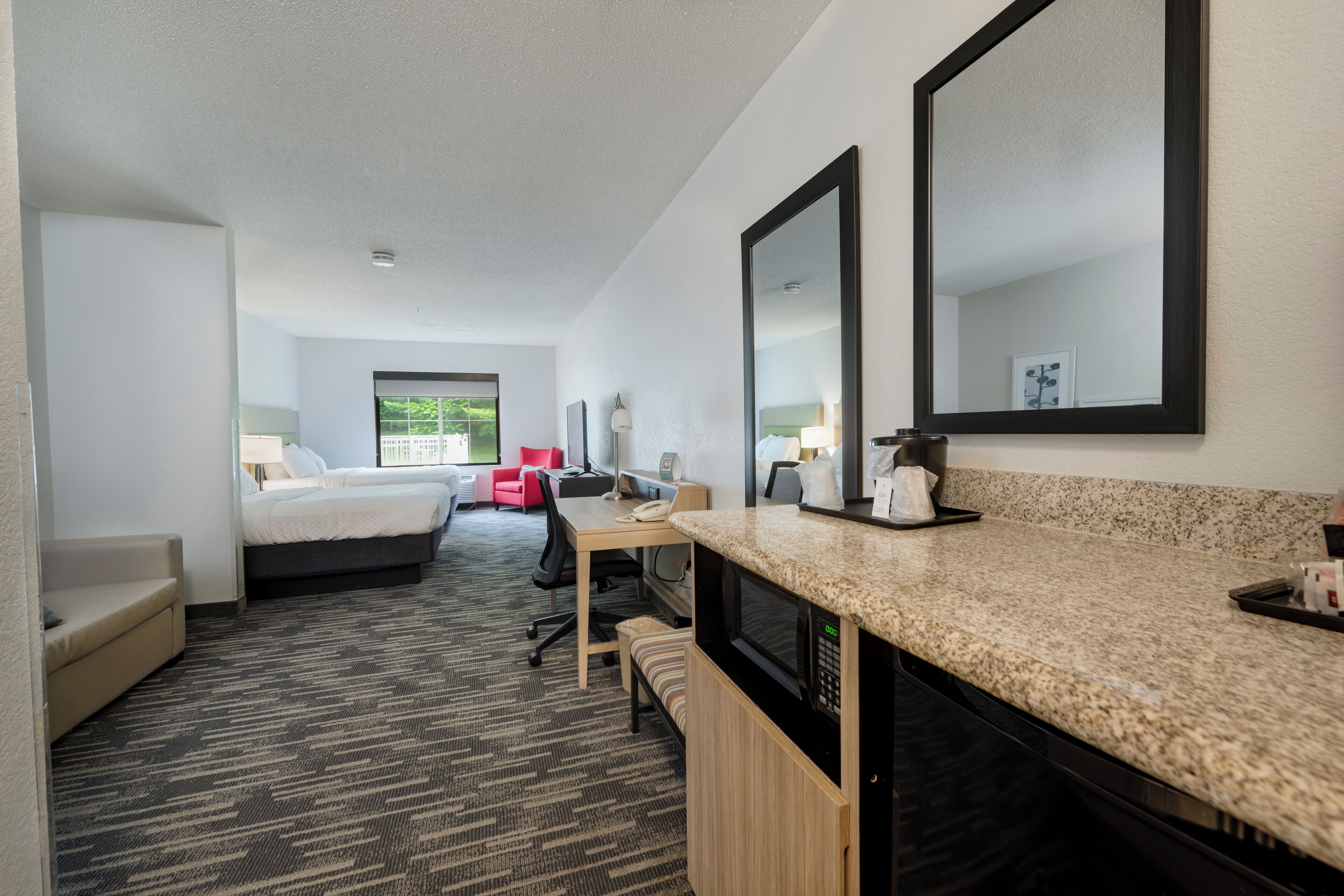 A hotel room with a bed, a desk, a microwave, a coffee maker, and a large mirror.