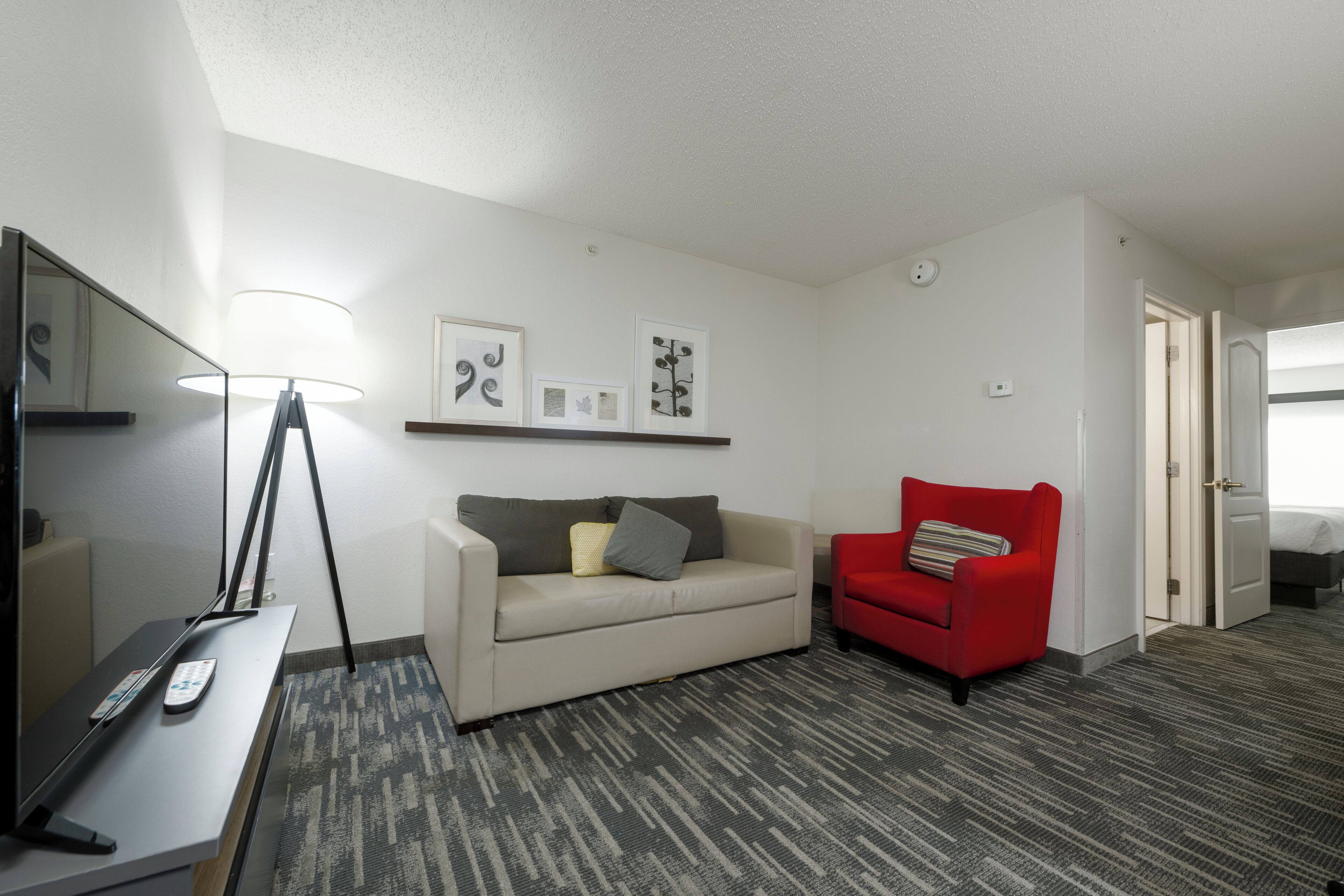 A hotel room with a sofa, a red armchair, a TV, and a lamp.