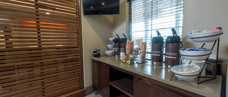 Una cocina moderna con un panel divisor de madera, un televisor de pantalla plana y una barra de desayuno con diferentes alimentos y recipientes.