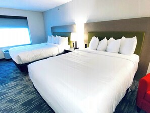 A hotel room with two beds, a red chair, and a large window.