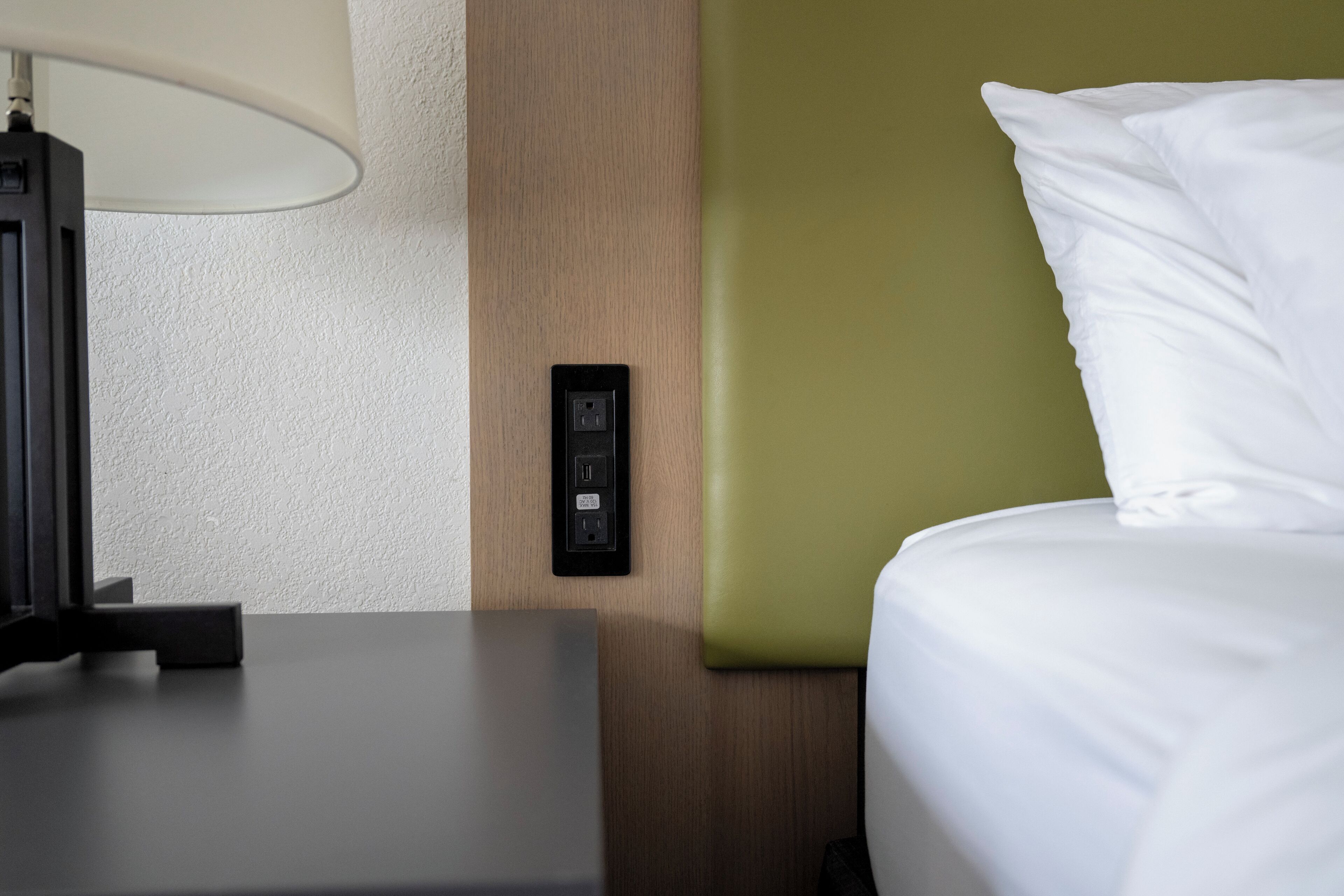 A hotel room with a bed, a nightstand, a lamp, and a wall socket.