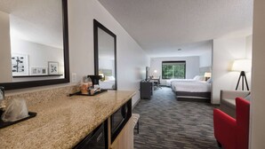 Hotelkamer met kitchenette, een bed, bureau, stoel en een grote spiegel.