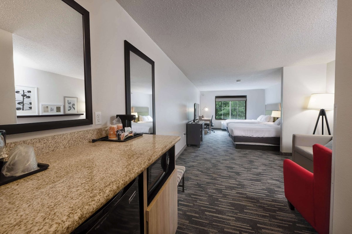 A hotel room with a kitchenette, a bed, a desk, a chair, and a large mirror.