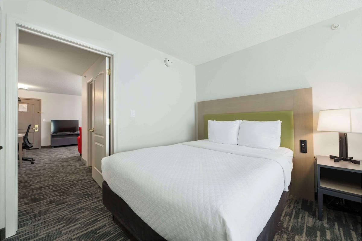 A hotel room with a large bed, a desk, a chair, a TV, and a lamp.