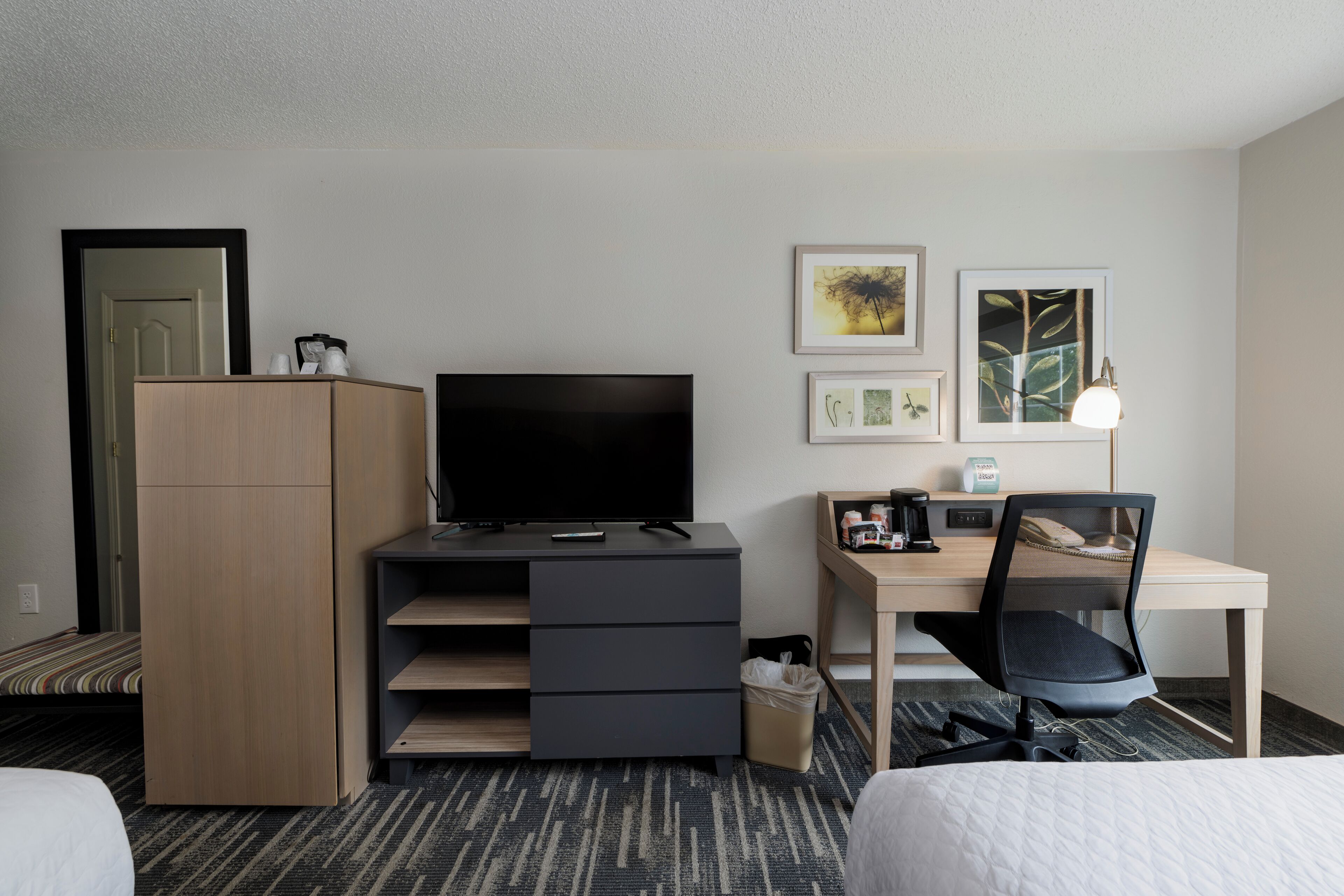 A hotel room with a bed, a desk with a computer, a TV, a wardrobe, and a trash bin.